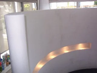 Καμπύλη λευκή κατασκευή τοίχου με στενή φωτισμένη οριζόντια εσοχή.