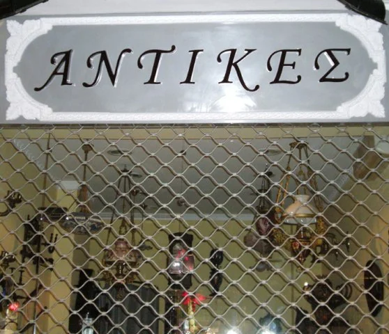 Διακοσμητική επιγραφή με τη λέξη «ΑΝΤΙΚΕΣ» μέσα σε ανάγλυφο λευκό πλαίσιο.